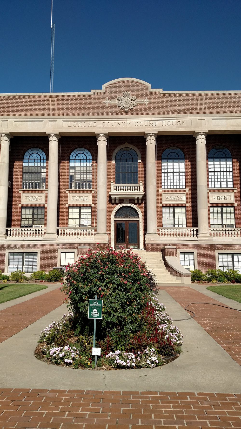 The front entrance of the Lonoke County Courthouse with flower beds blooming in the foreground.