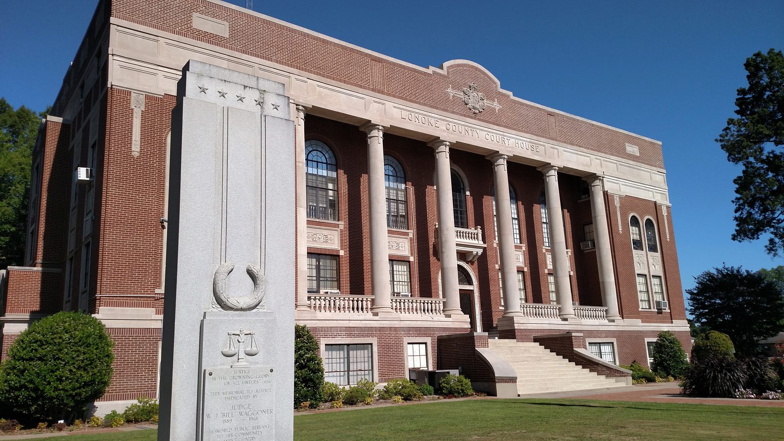 The Lonoke County Courthouse with a veterans and justice memorial monument on the front lawn.